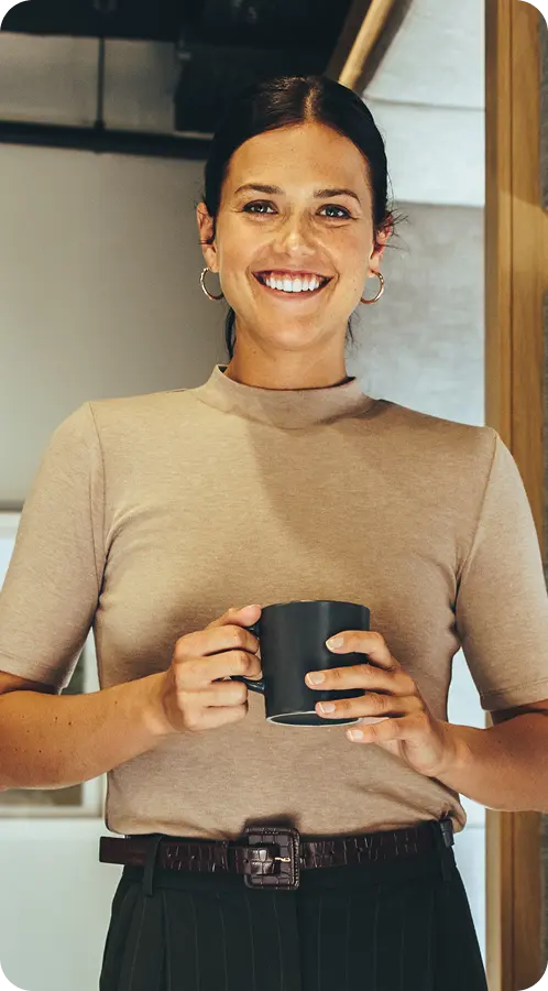 Smiling woman holding a coffee mug, representing a welcoming and professional atmosphere in a recovery center marketing context.