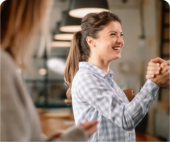 Smiling woman in a checkered shirt engaging in a handshake, symbolizing partnership and collaboration in recovery marketing.
