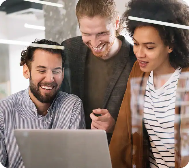 Three professionals collaborating and smiling while reviewing a laptop, symbolizing teamwork in implementing local SEO strategies for recovery centers.