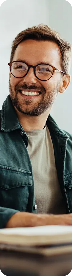 Smiling man with glasses wearing a green jacket, sitting at a desk, representing professional support for recovery center marketing.
